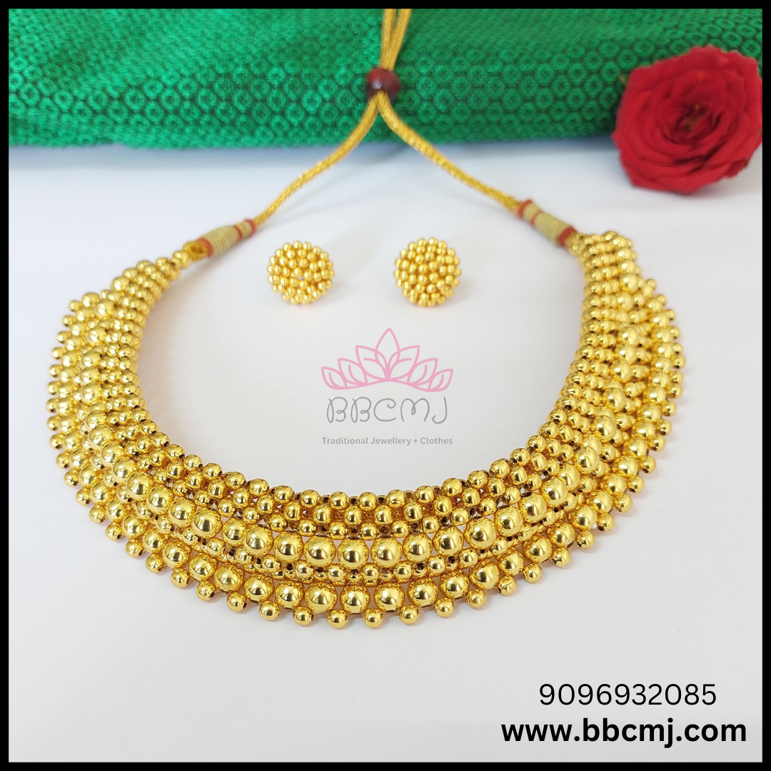 A gold-colored bead necklace and earrings set, displayed on a white surface with a green and red cloth in the background.