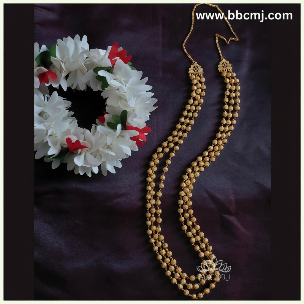 A gold-coated mohanmaal (a type of Indian beaded necklace) with a floral pattern, displayed next to a white and red flower wreath, against a dark background.